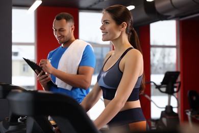 Photo of Happy trainer writing down workout plan while woman doing exercise in modern gym, space for text