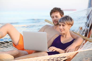 Young couple resting with laptop in hammock on beach