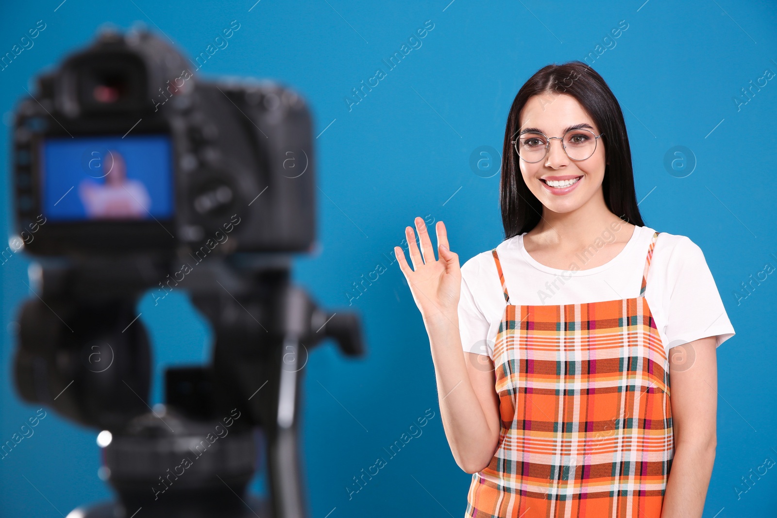 Photo of Young blogger recording video on camera against blue background