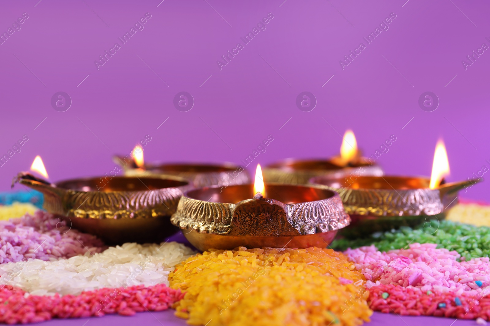 Photo of Diwali celebration. Diya lamps and colorful rangoli on purple background, closeup