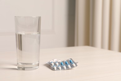 Different pills in blisters and glass of water on white wooden table. Space for text