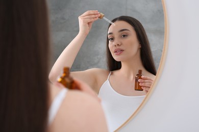 Photo of Woman applying essential oil onto face near mirror
