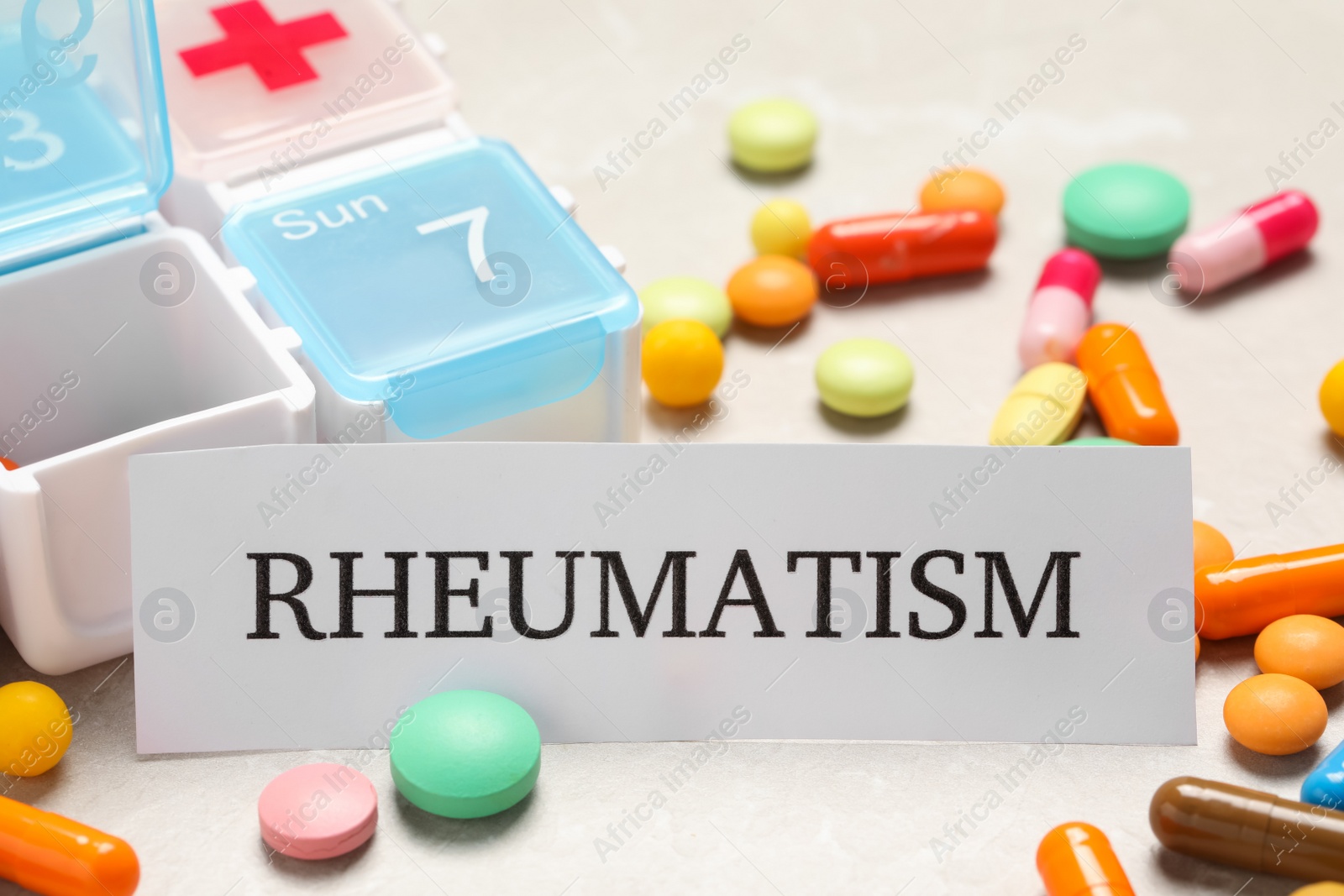 Photo of Card with word Rheumatism and pills on table, closeup
