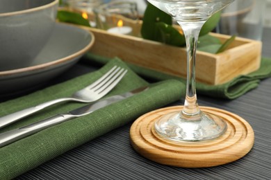 Place setting with glass and drink coaster on black wooden table, closeup view