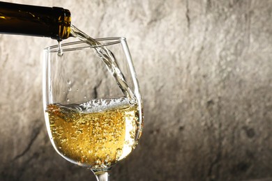 Pouring white wine into glass against grey background, closeup. Space for text