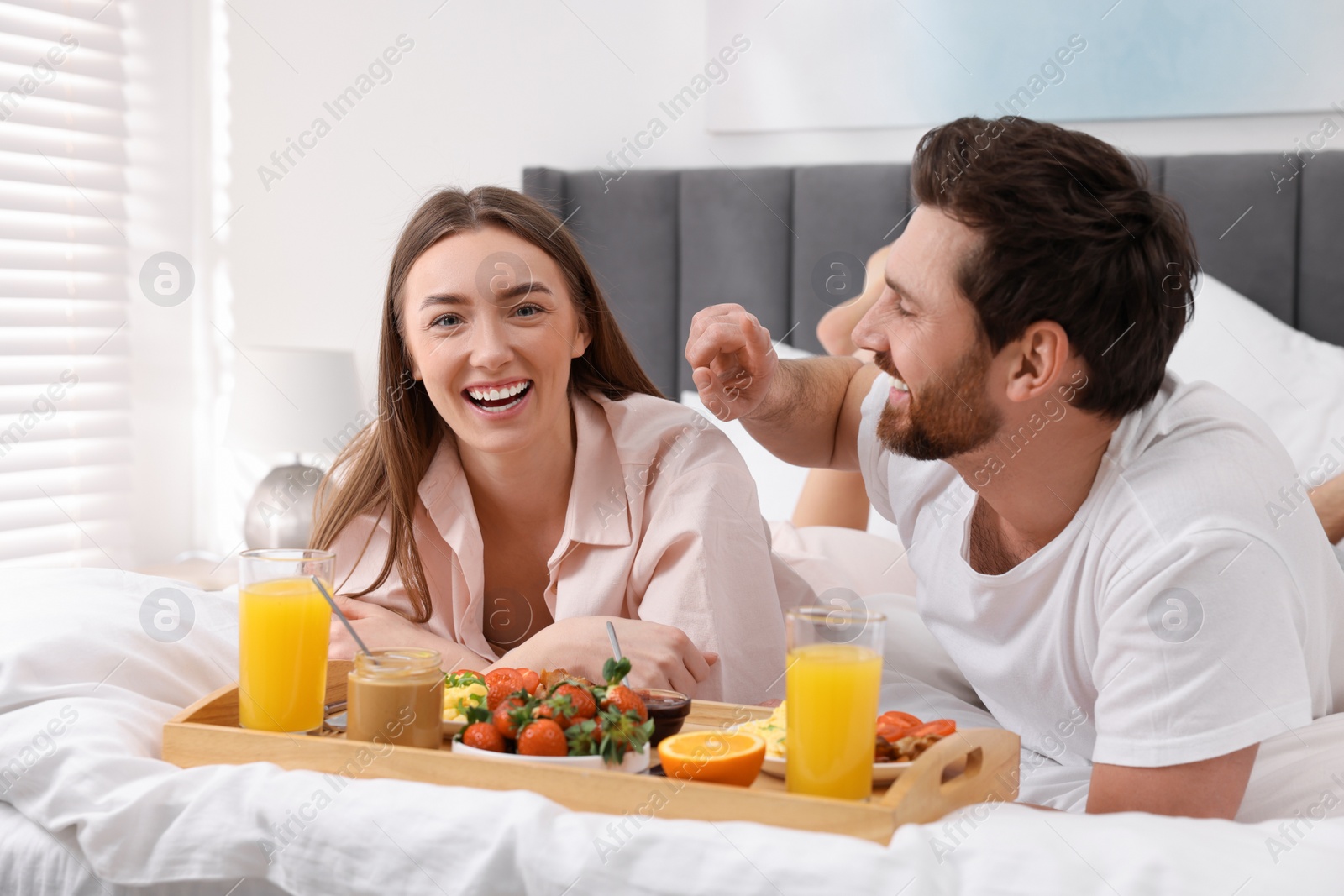 Photo of Happy couple eating tasty breakfast on bed at home