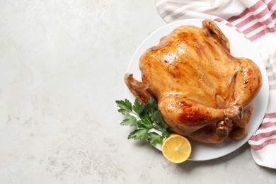 Photo of Tasty roasted chicken with parsley and lemon on light grey table, top view. Space for text