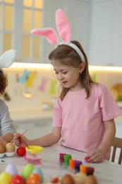 Photo of Easter celebration. Children with bunny ears painting eggs at white marble table in kitchen