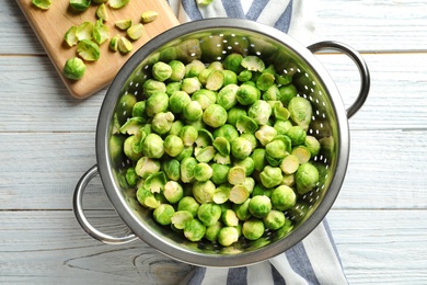 Photo of Colander with Brussels sprouts and napkin on wooden background, top view