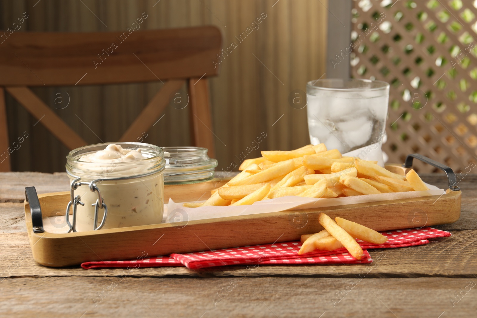 Photo of Delicious french fries served with sauce and glass of water on wooden table