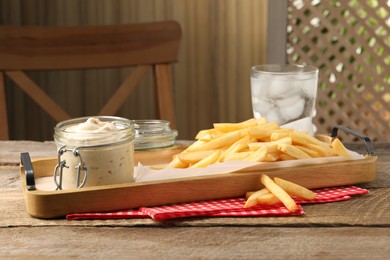 Delicious french fries served with sauce and glass of water on wooden table