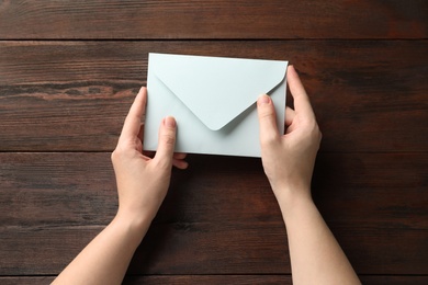 Photo of Woman with white paper envelope at wooden table, top view