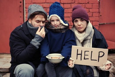 Photo of Poor young family with HELP sign on dirty street