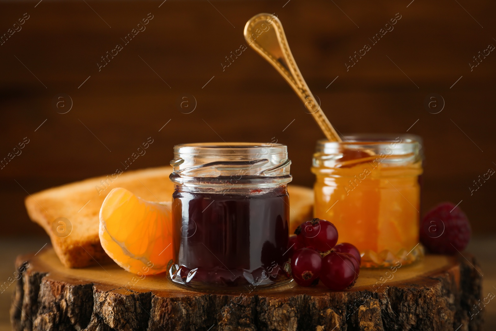 Photo of Jars with different sweet jams and ingredients on wooden stump