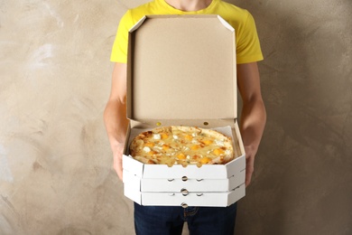 Young man with opened pizza box on color background. Food delivery service