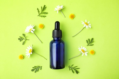Photo of Bottle of essential oil and flowers on color background, flat lay