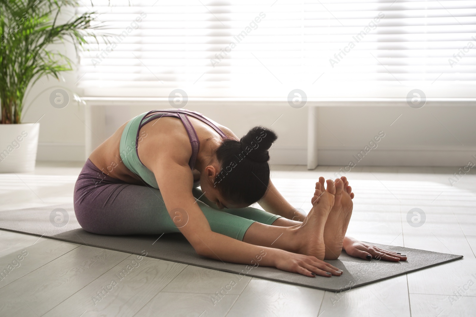 Photo of Woman practicing seated forward bend asana in yoga studio. Paschimottanasana pose