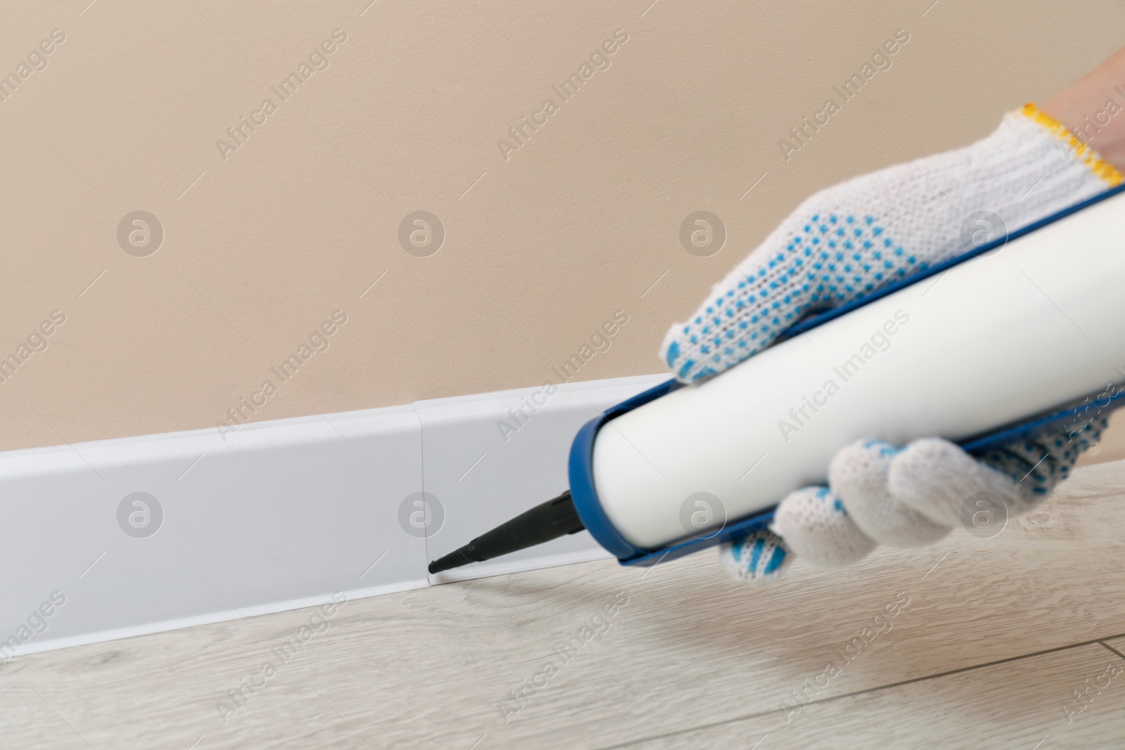 Photo of Man glueing plinth with caulking gun in room, closeup