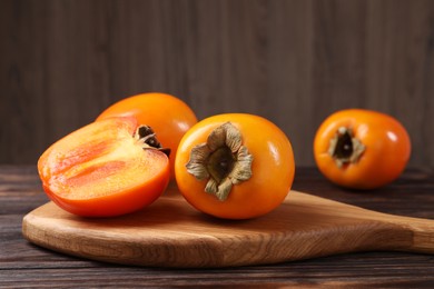 Photo of Whole and cut delicious ripe persimmons on wooden table