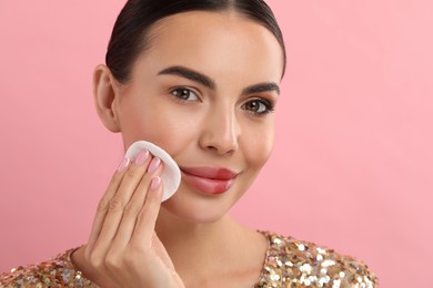 Beautiful woman removing makeup with cotton pad on pink background. Space for text