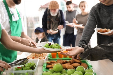 Volunteers giving food to poor people indoors