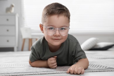 Photo of Cute little boy in glasses on floor at home