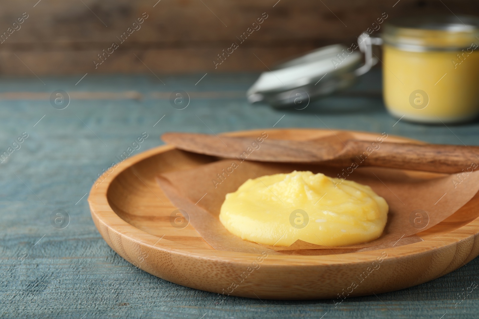 Photo of Plate and knife with Ghee butter on light blue wooden table, closeup.