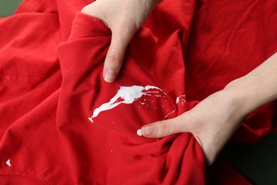 Photo of Woman holding red shirt with white paint stain, closeup