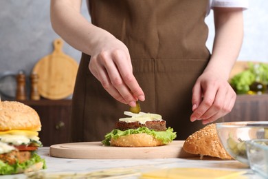 Photo of Woman making delicious vegetarian burger at white marble table, closeup