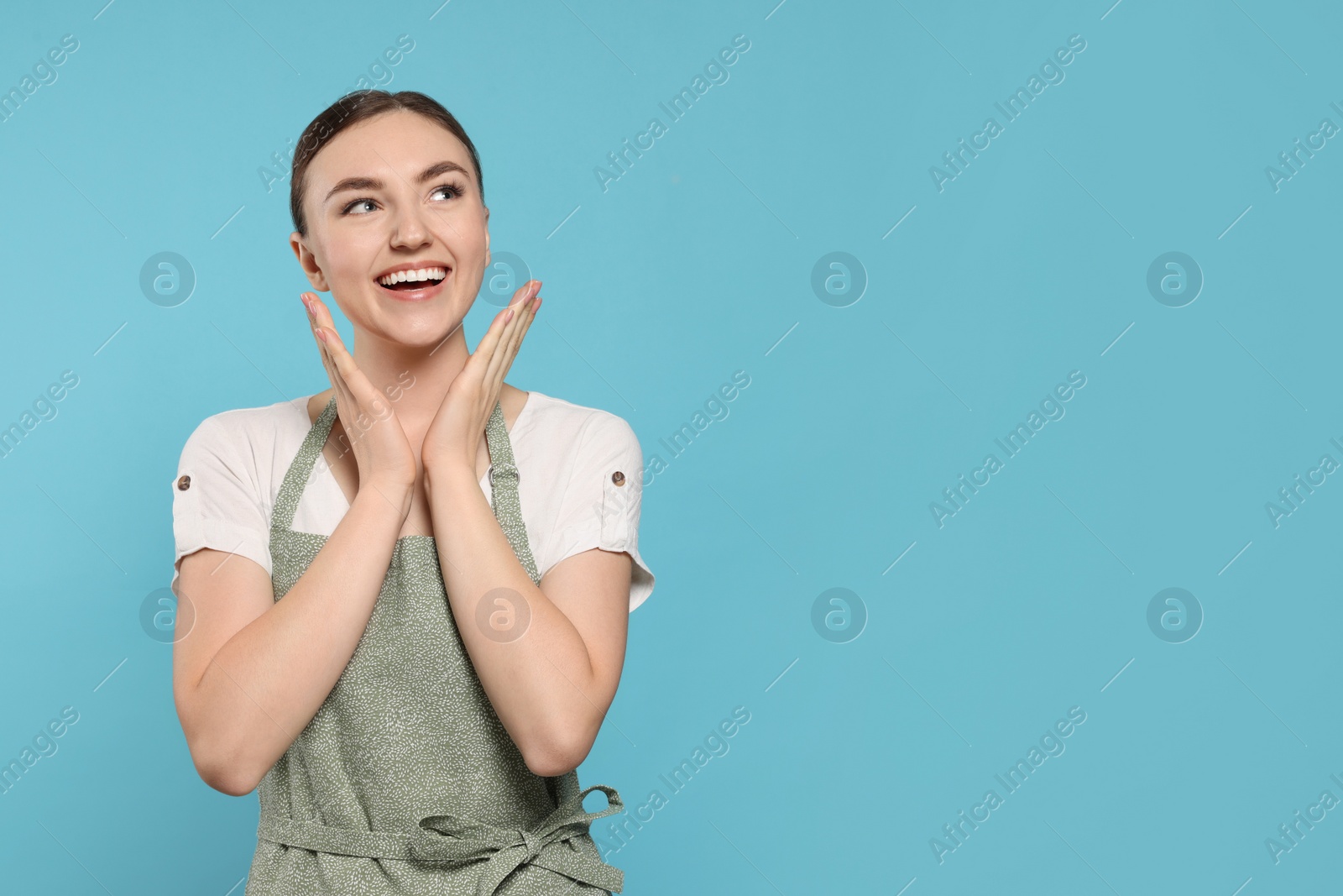 Photo of Beautiful young woman in clean apron with pattern on light blue background. Space for text