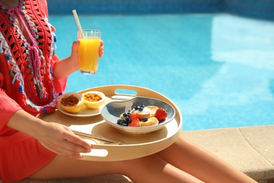 Young woman with delicious breakfast on tray near swimming pool, closeup. Space for text