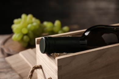 Photo of Open wooden crate with bottle of wine on blurred background