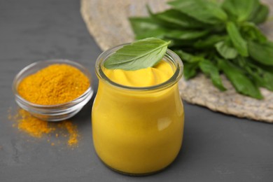 Photo of Tasty curry sauce, powder and basil leaves on grey table