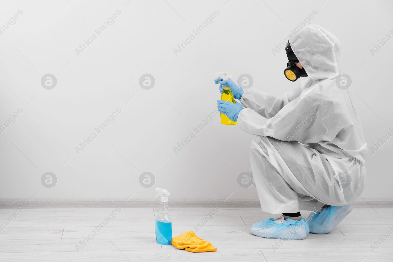 Photo of Woman in protective suit cleaning mold with sprayer on wall indoors