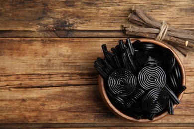 Photo of Tasty black candies and dried sticks of liquorice root on wooden table, flat lay. Space for text