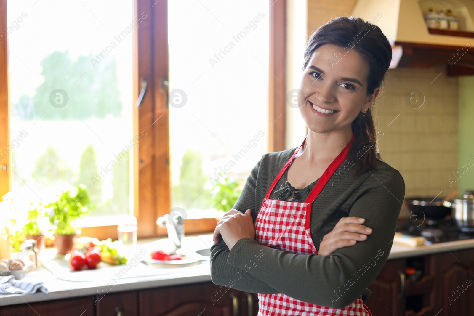 Photo of Portrait of happy young woman wearing apron in kitchen, space for text