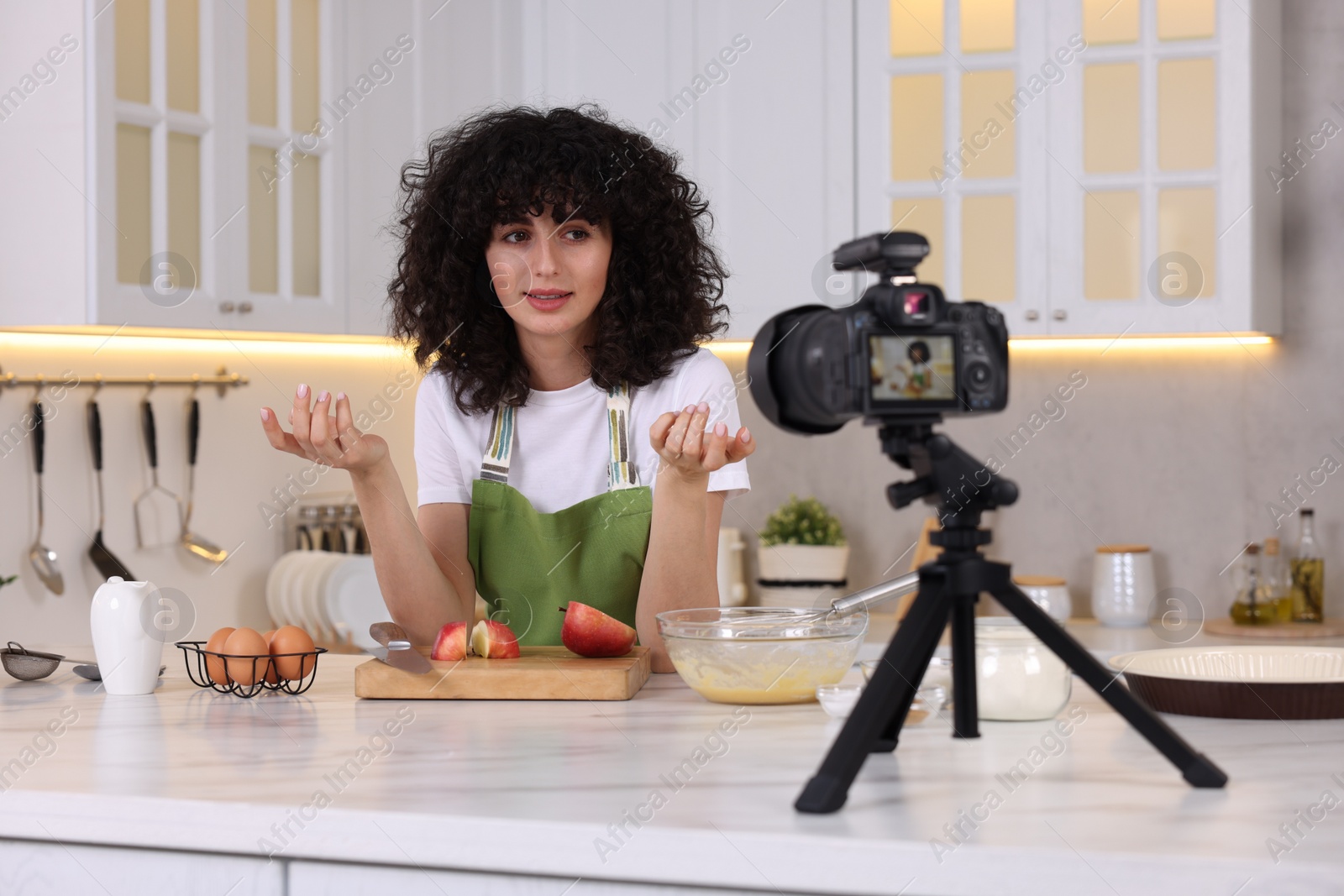 Photo of Smiling food blogger explaining something while recording video in kitchen