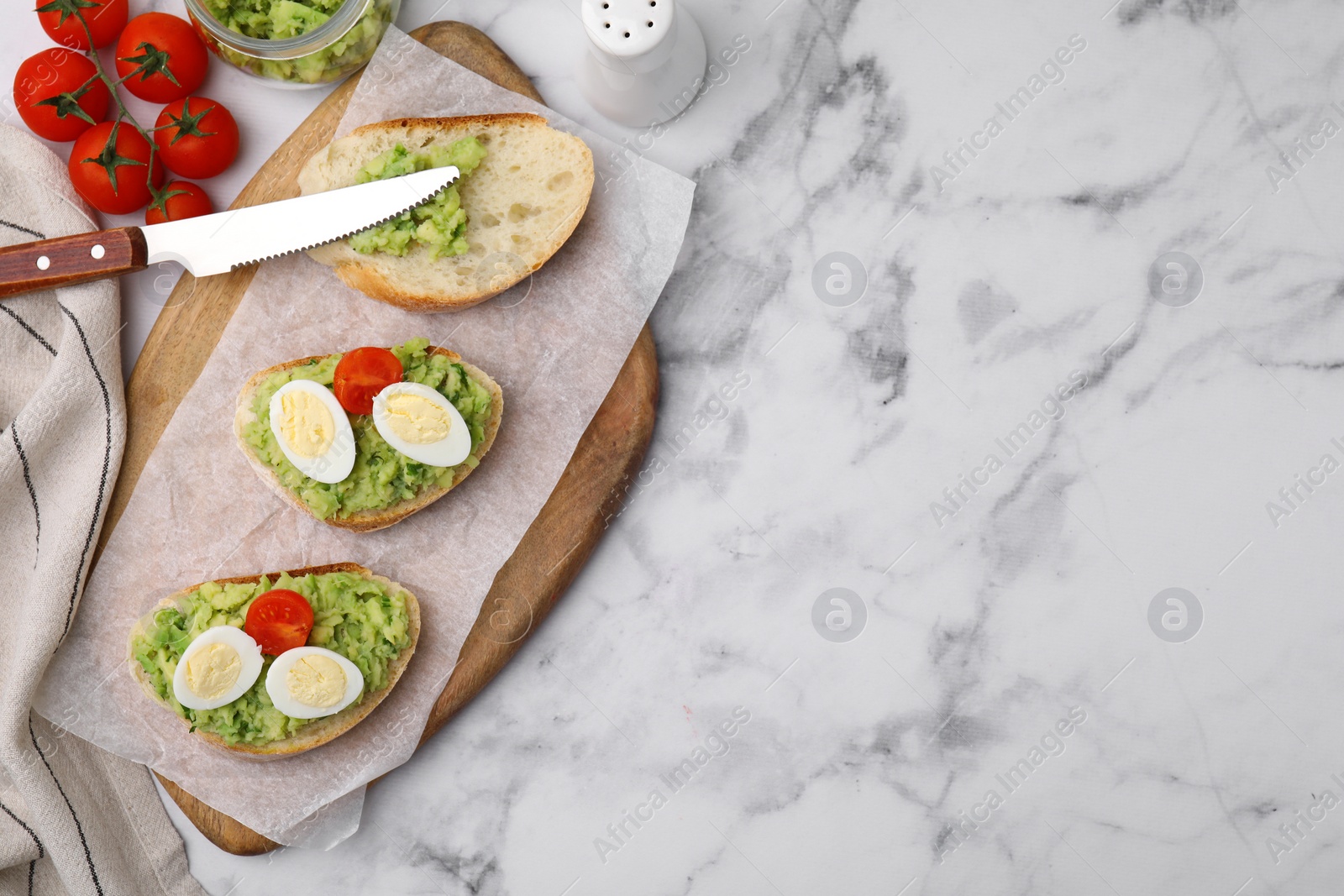 Photo of Delicious sandwiches with guacamole, eggs and tomatoes on white marble table, flat lay. Space for text