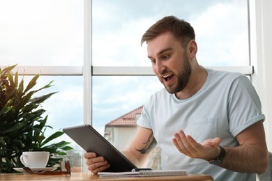 Photo of Emotional man participating in online auction using tablet at home