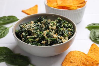 Photo of Tasty spinach dip with egg in bowl and nachos chips on white table, closeup