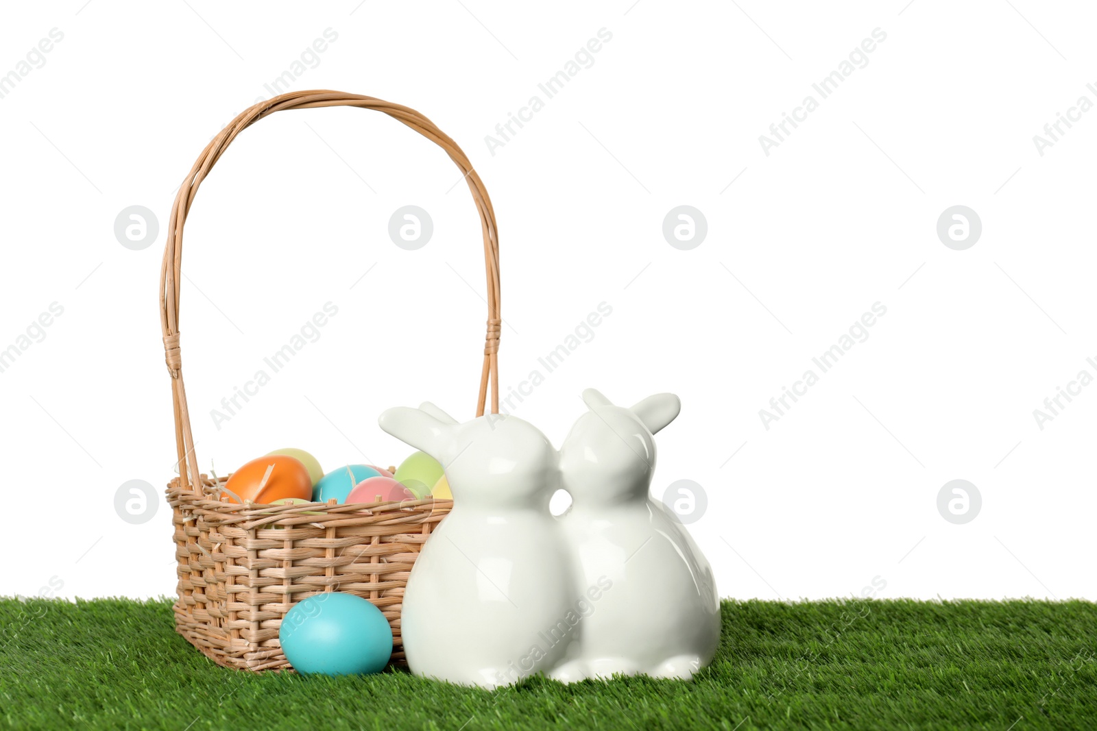 Photo of Ceramic Easter bunnies and dyed eggs on green grass against white background, space for text