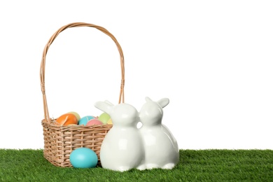 Photo of Ceramic Easter bunnies and dyed eggs on green grass against white background, space for text