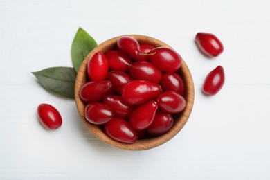 Photo of Fresh ripe dogwood berries with green leaves on white wooden table, flat lay