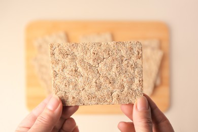 Photo of Woman holding fresh crunchy crispbread above table, top view