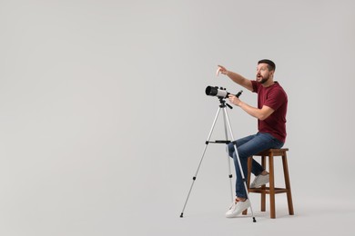 Photo of Excited astronomer with telescope pointing at something on light grey background. Space for text