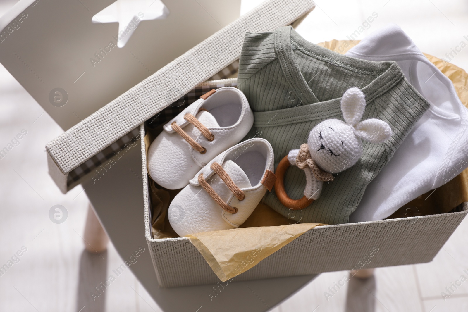 Photo of Box with baby clothes, shoes and toy on chair indoors, above view