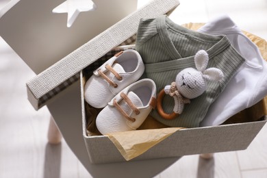 Box with baby clothes, shoes and toy on chair indoors, above view