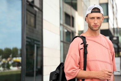 Photo of Handsome young man with stylish cap and backpack near building outdoors, space for text