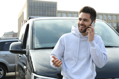 Photo of Handsome young man talking on phone near modern car outdoors