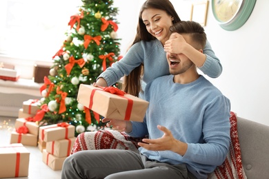 Young woman surprising her boyfriend with Christmas gift at home